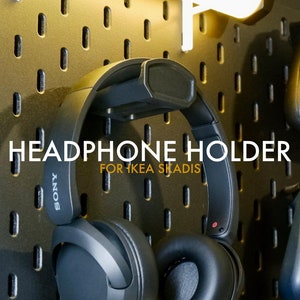 May include: A black headphone holder designed for IKEA's SLÄDIS pegboard. The holder is shown with a pair of black headphones hanging on it. The text "HEADPHONE HOLDER FOR IKEA SLÄDIS" is printed on the pegboard.