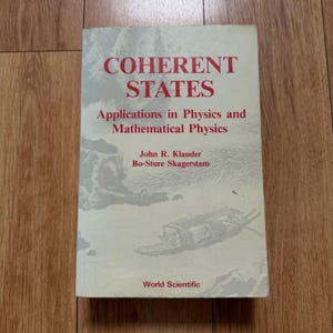Peut inclure: Un livre à couverture souple intitulé Coherent States: Applications in Physics and Mathematical Physics par John R. Klauder et Bo-Sture Skagerstam. La couverture est gris clair avec du texte rouge et une illustration pâle d'un bateau.