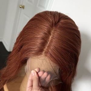 May include: A reddish-brown wig with long, flowing hair. The wig features a lace front and is styled with a natural part. The hair is a warm, vibrant color, and the wig is displayed on a mannequin head.