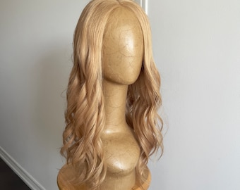 May include: A long, wavy, light blonde wig on a mannequin head. The wig is styled in loose waves and has a natural-looking finish.
