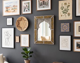 May include: A gallery wall featuring a collection of framed art prints, a woven basket, a rectangular mirror with an arched top and gold-toned frame, and a botanical illustration, all arranged on a dark gray wall above a wooden console table.
