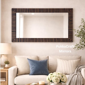 May include: Rectangular mirror with a dark brown and black striped frame, hanging above a white sofa with decorative pillows. The mirror reflects the room. The text "PukkaCraft Mirrors" is visible.