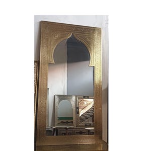 May include: A large, ornate gold-colored mirror with an arched top and intricate etched detailing. The mirror has a rectangular shape and is likely a decorative piece for a home. Other smaller mirrors are visible in the background.