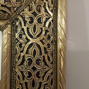 May include: A rectangular mirror frame featuring a metallic gold finish with intricate, raised floral and scrollwork patterns set against a recessed black background. The outer edge has a twisted rope texture, and the inner border is lined with small, evenly spaced metallic studs.