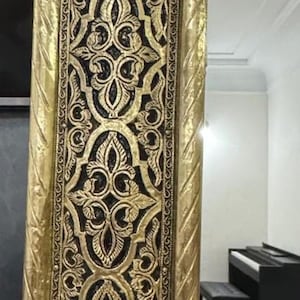 May include: A tall rectangular mirror featuring a wide, ornate gold-colored frame with intricate black recessed detailing. The frame displays repeating symmetrical floral and leaf-like patterns, bordered by a twisted rope-style edge design.