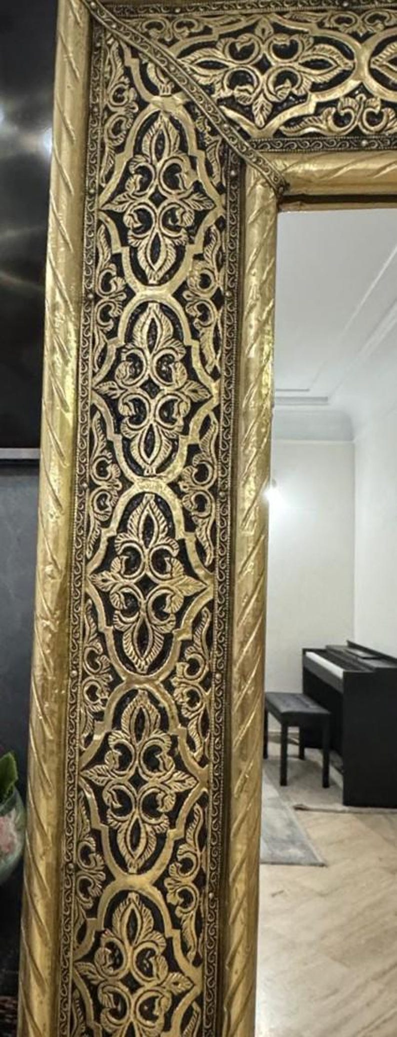 May include: A tall rectangular mirror featuring a wide, ornate gold-colored frame with intricate black recessed detailing. The frame displays repeating symmetrical floral and leaf-like patterns, bordered by a twisted rope-style edge design.