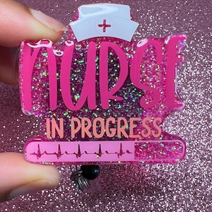Puede incluir: Porta credencial de purpurina rosa con un gorro de enfermera y el texto "Nurse in Progress" con un gráfico de latido del corazón.