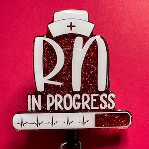 Puede incluir: Portagafete rojo con purpurina con una gorra de enfermera blanca, las letras "RN" y el texto "IN PROGRESS" con una barra de progreso y un gráfico de latido del corazón.