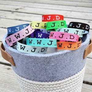May include: A basket filled with colorful woven bracelets with the letters "W.J.D." printed on them.