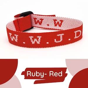 May include: Ruby-red woven strap with white text reading ".W.J.D." and a black buckle. The strap is folded over itself. The text "Ruby-Red" is in a red banner at the bottom.