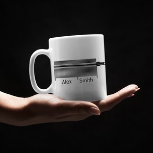 K&ouml;nnte beinhalten: Wei&szlig;e Keramiktasse mit einer schwarzen Grafik einer Schallwelle und dem Text "Alex Smith".