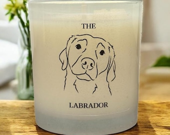 Op de afbeelding: Een kaars van matglas met een zwarte lijntekening van het gezicht van een Labrador. De tekst "THE LABRADOR" is onder de hondenillustratie gedrukt. De kaars staat op een houten oppervlak.