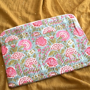 Può includere: Una pochette rettangolare trapuntata con un motivo floreale. La pochette presenta uno sfondo azzurro con fiori rosa e bianchi e foglie verdi. La pochette è su un tessuto color oro.