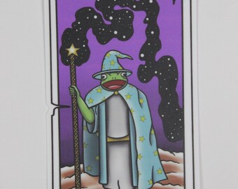 May include: A tarot card with a purple background and a green frog wearing a blue robe and a wizard's hat. The frog is holding a staff with a star on top. The card reads "THE WIZARD."