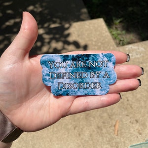 May include: A blue and white sticker with the text "You are not defined by a disorder".