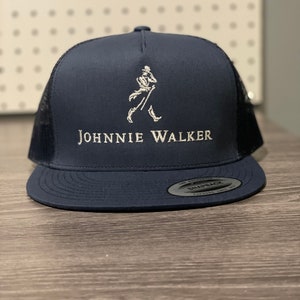 May include: A navy blue trucker hat with a white mesh back. The hat has a white embroidered logo of a walking man and the text "JOHNNIE WALKER".