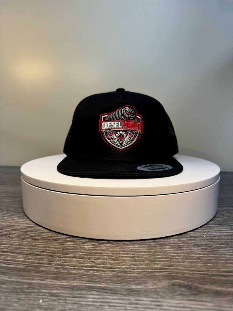 Pode incluir: Bon&eacute; snapback preto com o logotipo Diesel Power. O logotipo apresenta um design de escudo vermelho e branco com o texto "DIESEL POWER" e um gr&aacute;fico de um motor. O bon&eacute; &eacute; exibido em um suporte circular branco.