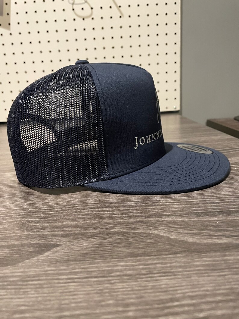 May include: A navy blue trucker hat with a mesh back and a white embroidered logo that says "JOHNNIE".