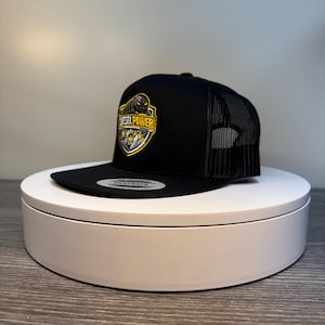 Pode incluir: Bon&eacute; snapback preto com parte traseira em rede e aba reta. A frente apresenta um emblema amarelo e preto com as palavras "DIESEL POWER". O bon&eacute; &eacute; exibido em um suporte circular branco.