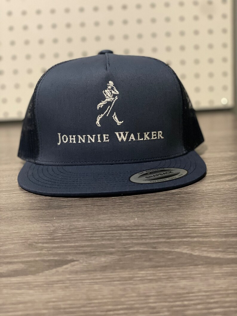 May include: A navy blue trucker hat with a white mesh back. The hat features a white embroidered Johnnie Walker logo with a walking man figure.