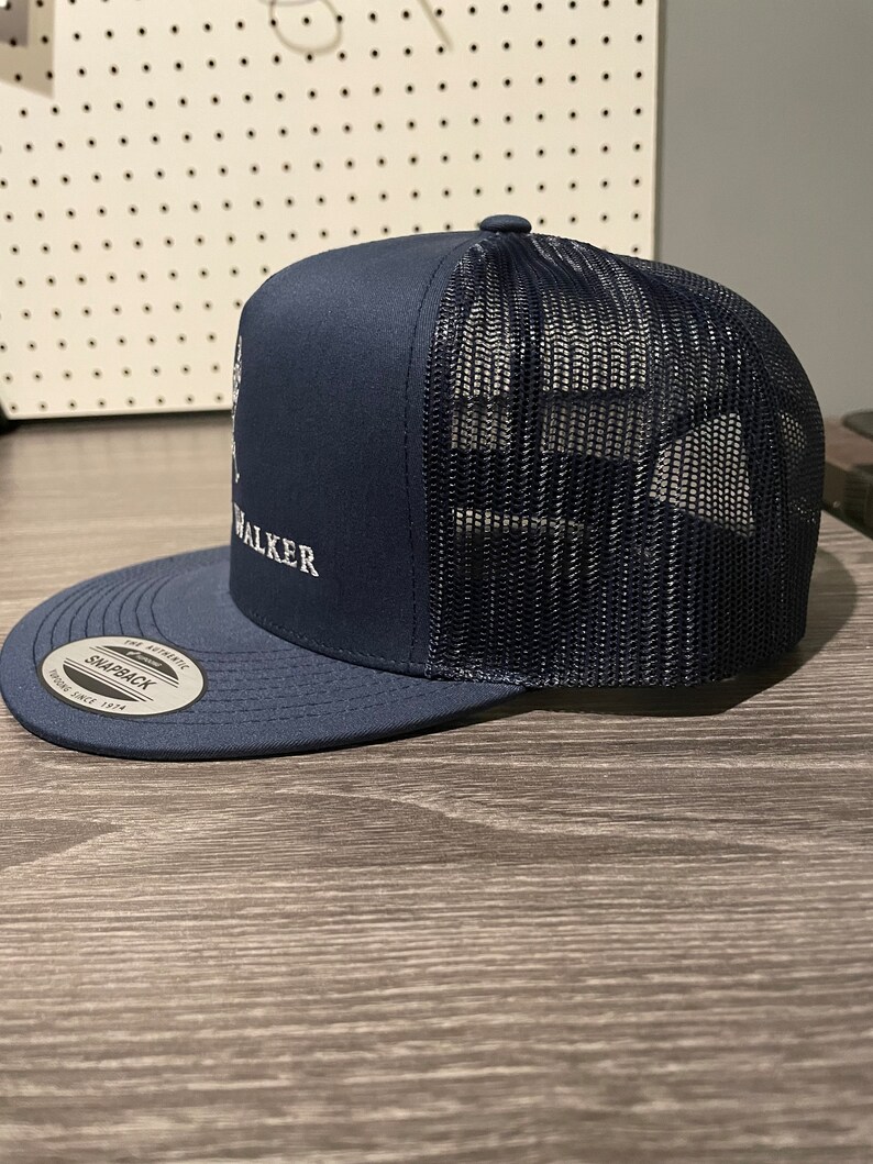 May include: A navy blue trucker hat with a black mesh back. The hat has a white embroidered logo that says "WALKER" on the front.