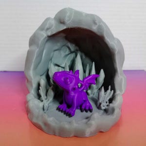 May include: A purple dragon figurine sitting inside a grey 3D printed cave with rock formations.