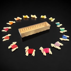 Puede incluir: Una caja de madera con 12 ranuras para guardar hilo, rodeada de 12 figuras de llama de madera, cada una con un color de hilo diferente envuelto alrededor.
