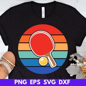 May include: A black t-shirt with a retro-style design featuring a table tennis bat and ball on a rainbow background. The text "PNG EPS SVG DXF" is at the bottom of the image.