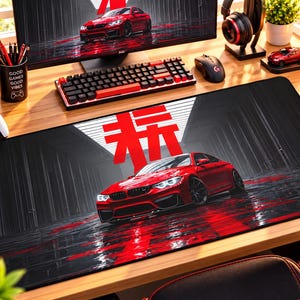 May include: A rectangular desk mat featuring a red sports car parked on a dark, reflective surface. Above the car, a large red Japanese kanji character is displayed against a white background. The design includes dark, vertical lines.