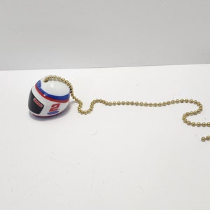 May include: A white, blue, and red racing helmet charm with a gold chain. The helmet has the number 2 and the word "Ford" on it.