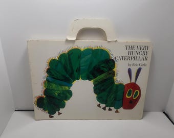 May include: A vintage copy of "The Very Hungry Caterpillar" by Eric Carle. The book cover features a green caterpillar with a red head and yellow eyes. The book is in a cardboard box with a handle.
