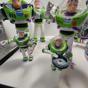 May include: Four different sized Buzz Lightyear action figures from the Toy Story franchise. The figures are all green, white, and purple with a space ranger design. The figures are all in different poses.
