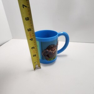 May include: A blue plastic mug with a handle. The mug has a 3D image of a brown gorilla on a green background. The mug is approximately 3 inches tall.