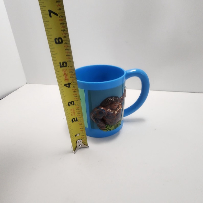 May include: A blue plastic mug with a handle. The mug has a 3D image of a brown gorilla on a green background. The mug is approximately 3 inches tall.