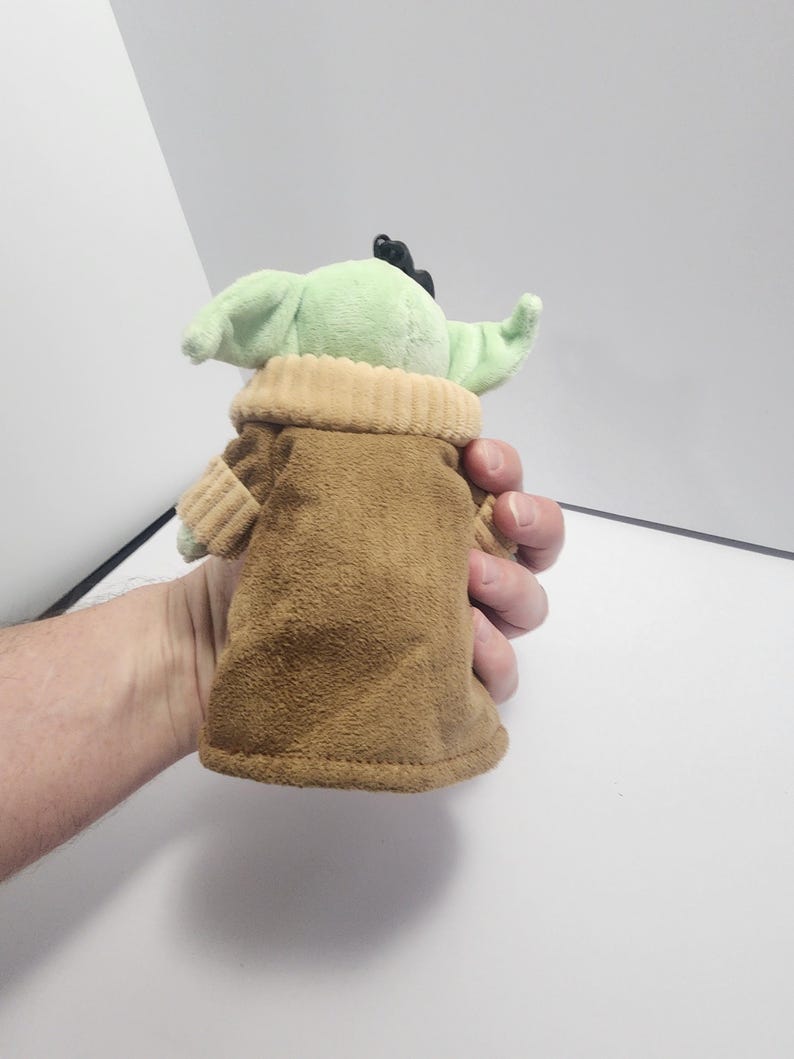 May include: A plush toy of a character with large green ears and a brown robe. The toy has a light green face and a tan collar. The character is from a popular science fiction franchise.