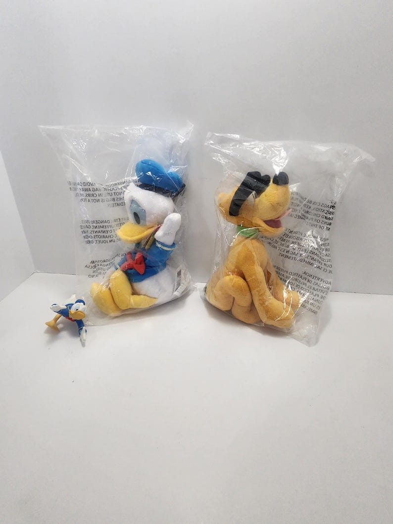 Pu&ograve; includere: Due peluche di personaggi Disney in confezioni di plastica. Uno &egrave; Paperino, con un costume e un cappello da marinaio blu, e l'altro &egrave; Pluto, un cane giallo con orecchie nere. &Egrave; presente anche una piccola statuina di Paperino.