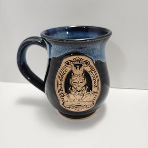 Peut inclure: Une tasse en céramique bleue avec un glaçage brun et un motif circulaire représentant un chevalier en armure, le texte "Kansas City Renaissance Festival" et l'année "1992".