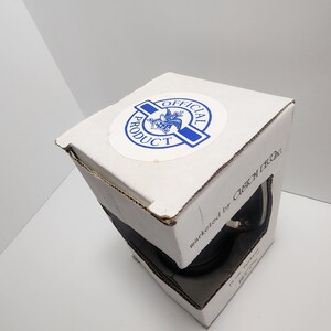 Puede incluir: Una caja blanca con una pegatina azul y blanca que dice "Producto Oficial" y un art&iacute;culo negro y plateado en su interior. La caja tambi&eacute;n dice "comercializado por Custom Decals".