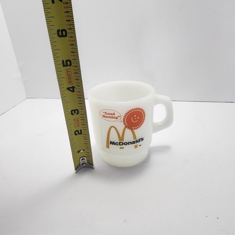 Puede incluir: Una taza de cer&aacute;mica blanca con un asa negra y el texto "But First, Coffee" en negro, con una fuente de estilo manuscrito. La taza est&aacute; sobre una superficie blanca.