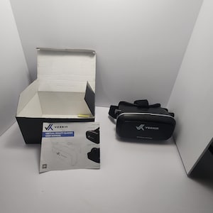 Puede incluir: Unos auriculares de realidad virtual VOXKIN negros con correas ajustables, un manual de usuario y una caja de cartón negra abierta. Los auriculares tienen el logotipo de VOXKIN en la parte delantera. El manual de usuario tiene el logotipo de VOXKIN y las palabras "VIRTUAL REALITY GLASSES USER MANUAL".
