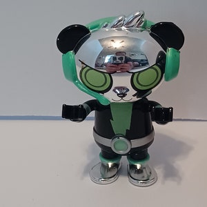 Puede incluir: Un panda de juguete plateado y negro que lleva unos auriculares verdes con un rayo verde en el pecho. El panda tiene ojos verdes y un mohawk plateado.