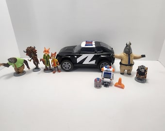 May include: A black police car with a white stripe and a blue light on top. There are several animal figurines, including a sloth, a buffalo, two foxes, a rhino, and a raccoon. The figurines are all standing on small bases.