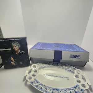 以下が含まれることがあります： 花柄の白い青いセラミック製サービングプラッターと「and you'll get cookies, lots of cookies」のテキスト。プラッターの後ろには「The Walking Dead Supply Drop」の箱があります。