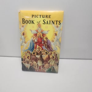 May include: A yellow book titled "Picture Book of Saints" with an illustration of religious figures. The cover art features a central figure surrounded by angels and other figures. The book is rectangular and appears to be new.
