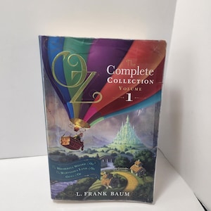 May include: The Complete Collection Volume 1 by L. Frank Baum. The book cover shows a colourful illustration of a hot air balloon, a yellow brick road, and the Emerald City. The title "OZ" is prominently displayed.