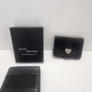 May include: Three black wallets and a black box are displayed against a white background. The box has the text "ACCESS DENIED" and the website address "www.rfiddenied.com". One wallet has a heart-shaped clasp.