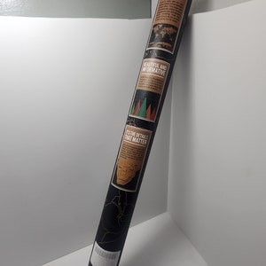 May include: A rolled-up black scratch-off world map with gold accents. The map features text that reads "Going to Travel, Scratch It", "Beautiful and Informative", and "It's the Details That Matter". The map is in a cylindrical shape.