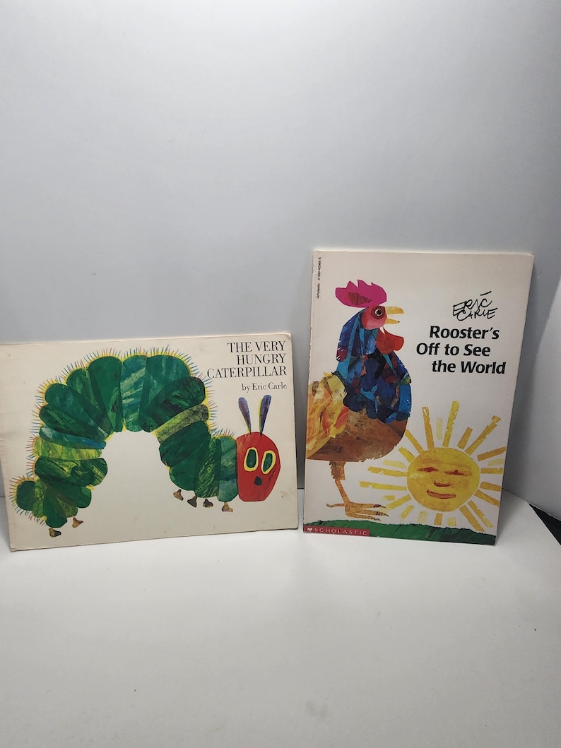 Puede incluir: Dos libros infantiles de Eric Carle. La Oruga Muy Hambrienta presenta una oruga verde con ojos rojos y una boca roja. El Gallo que Sale a Ver el Mundo presenta un gallo con una cresta roja y un sol amarillo.