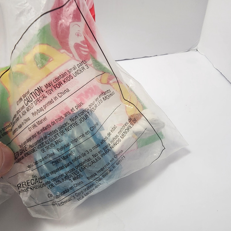 May include: A sealed plastic bag containing a blue toy. The bag has text in English and Spanish, including a warning about small parts and a caution for children under 3. The bag is printed in China.