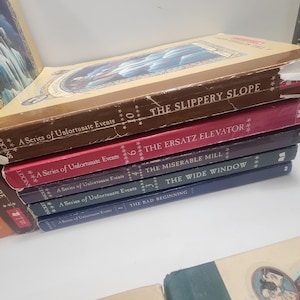 May include: A stack of hardcover books from "A Series of Unfortunate Events" by Lemony Snicket. The titles visible are "The Slippery Slope", "The Ersatz Elevator", "The Miserable Mill", "The Wide Window", and "The Bad Beginning". The books have colorful spines.